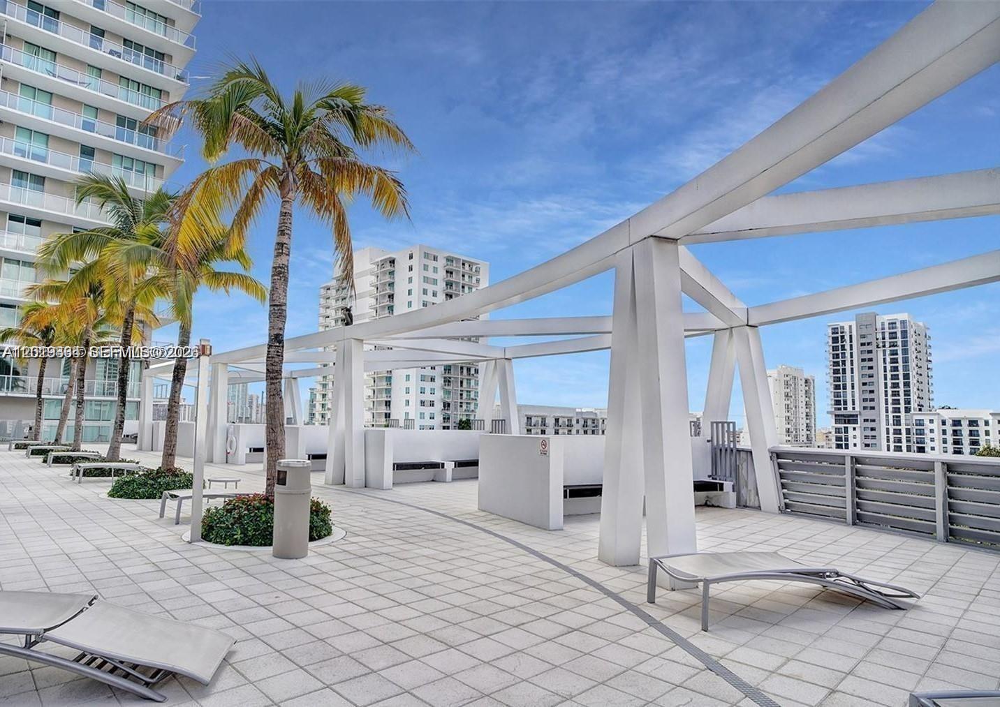 A rooftop terrace features white structural beams, palm trees, lounge chairs, and surrounding high-rise buildings — 1111 SW 1 ave # 2215, Miami FL 33130, MIAMI, FL