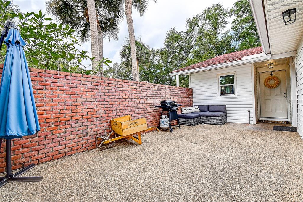 A patio features a brick wall, a wooden wheelbarrow, a grill, and outdoor seating — 1439 WATER VIEW DRIVE W, LARGO, FL