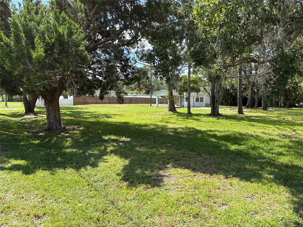 A grassy, tree-filled lot features a small white structure with a covered carport in back — 15127 BLUEFISH STREET, HUDSON, FL