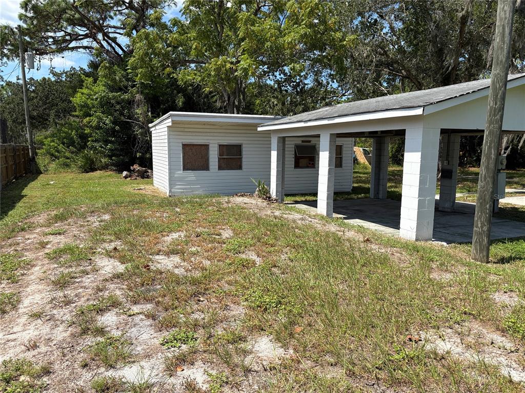 A white house with a carport and a small attached shed sits on a grassy lot — 15127 BLUEFISH STREET, HUDSON, FL