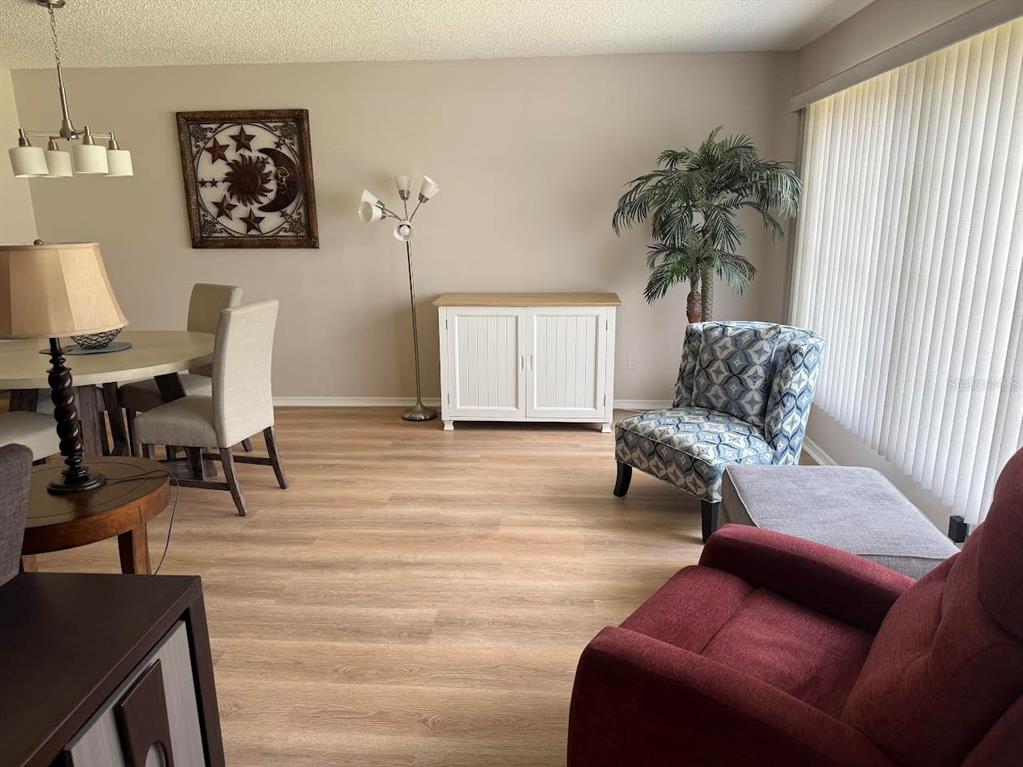 A dining and living area with light wood flooring, a white cabinet, and patterned chair — 508 FOXGLOVE CIRCLE UNIT B, SUN CITY CENTER, FL