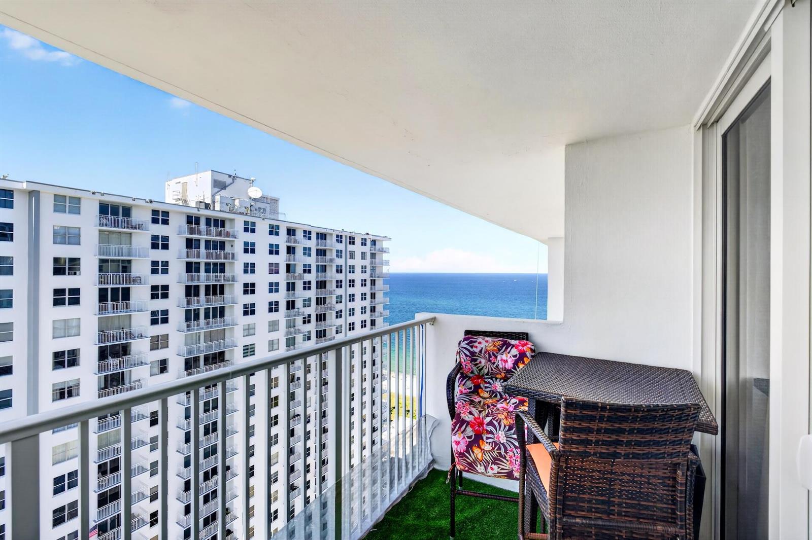 A balcony with a small table and chairs overlooks the ocean and a neighboring building — 111 Briny Avenue # 2711, Pompano Beach FL 33062, POMPANO BEACH, FL