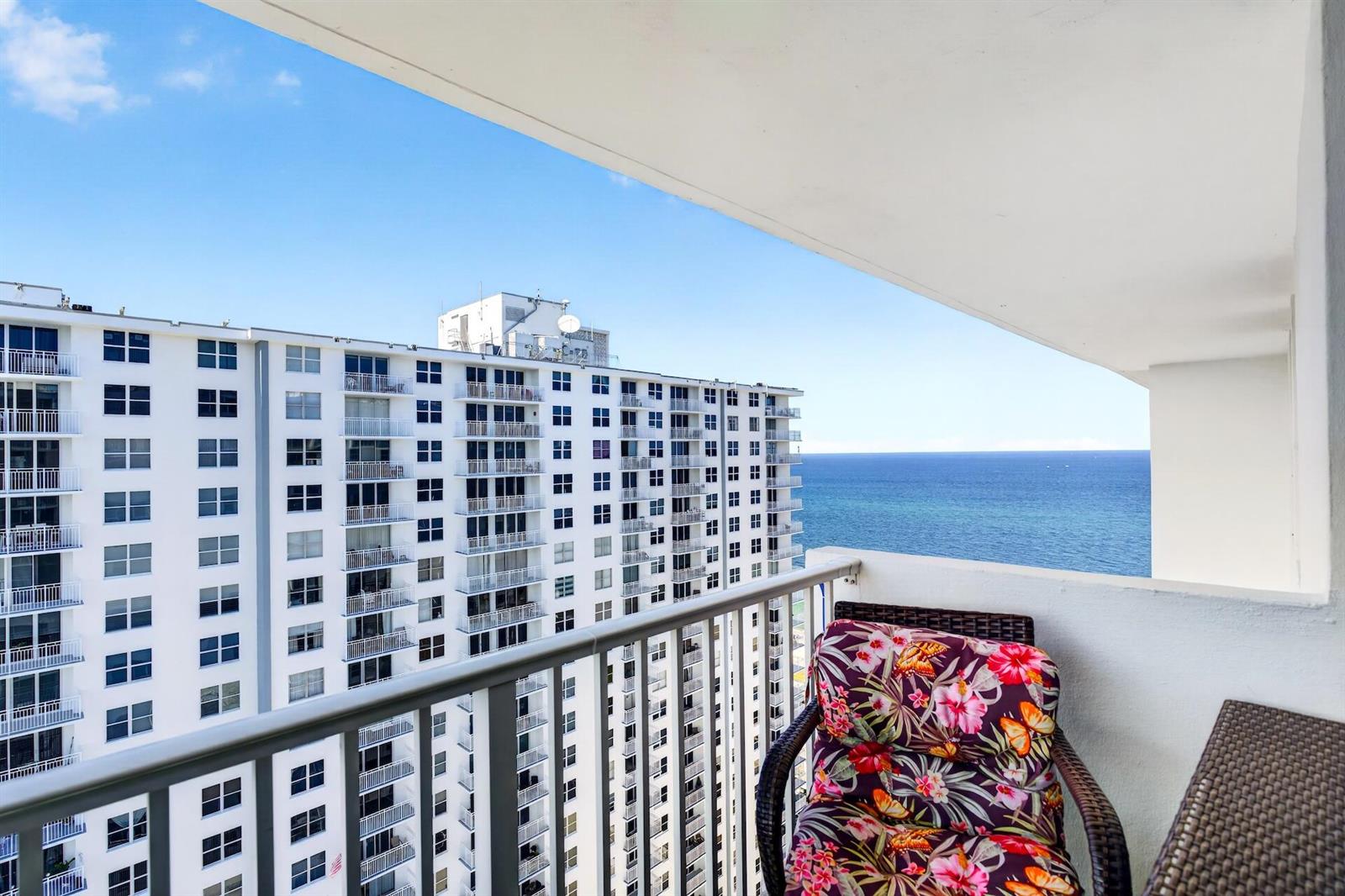 A balcony with a floral chair overlooks the ocean and a neighboring high-rise apartment building — 111 Briny Avenue # 2711, Pompano Beach FL 33062, POMPANO BEACH, FL