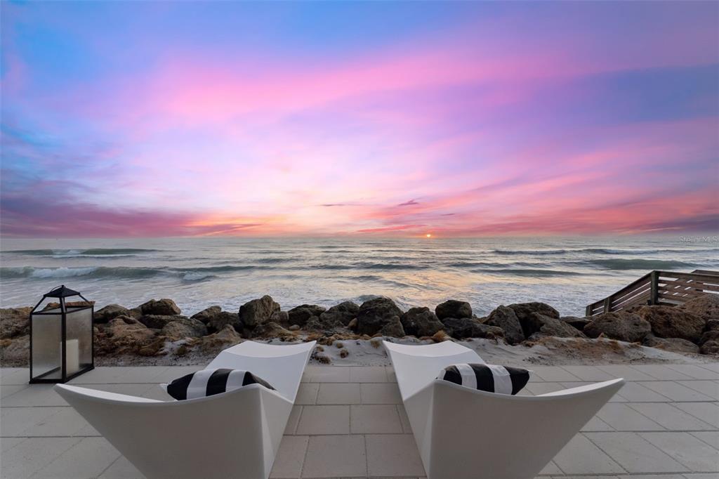 Two white lounge chairs sit on a patio overlooking a rocky shoreline and the ocean — 6887 S ATLANTIC AVENUE, NEW SMYRNA BEACH, FL