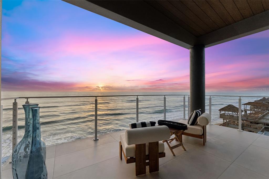 A balcony with modern lounge chairs overlooks the ocean during a colorful sunset — 6887 S ATLANTIC AVENUE, NEW SMYRNA BEACH, FL