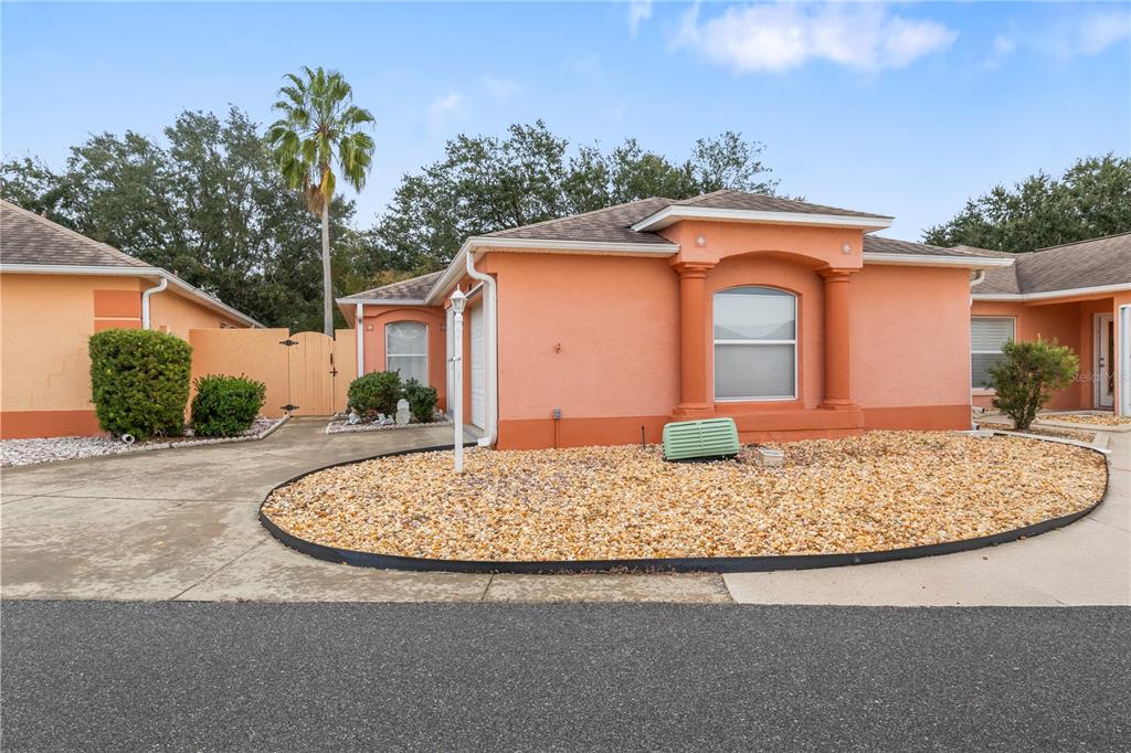 An exterior view of a peach-colored single-story house with a gravel front yard — 631 ENCONTO STREET, THE VILLAGES, FL