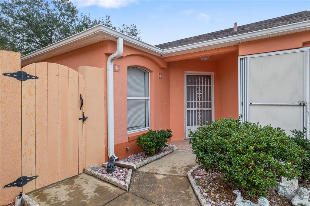 A peach-colored house exterior features a wooden gate, a window, and a screened front door — 631 ENCONTO STREET, THE VILLAGES, FL