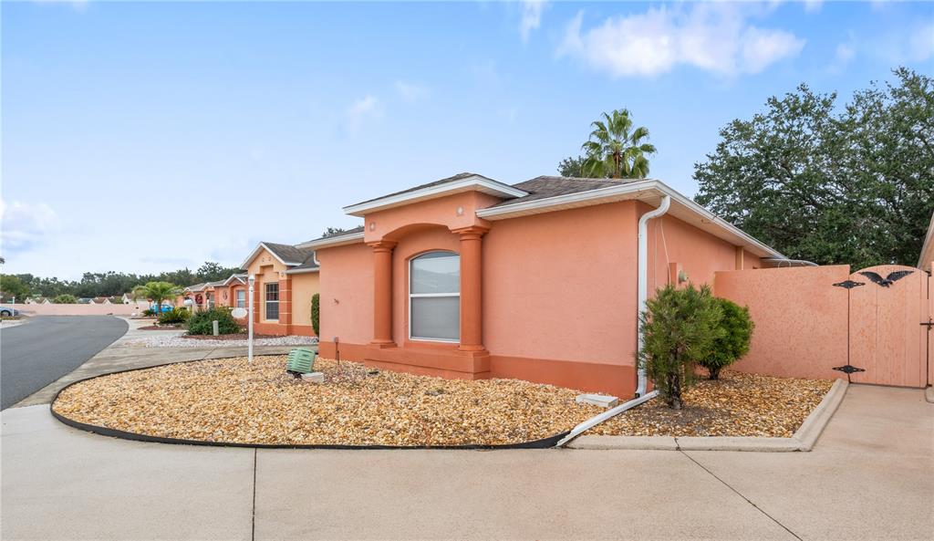 A peach-colored stucco house with a gravel front yard and a wooden privacy gate — 631 ENCONTO STREET, THE VILLAGES, FL