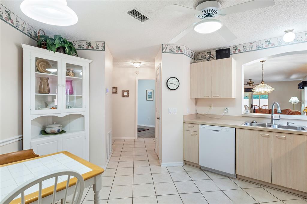 A kitchen with light wood cabinets, white appliances, tile flooring, and a dining area — 631 ENCONTO STREET, THE VILLAGES, FL