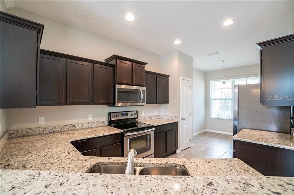 A kitchen features dark wood cabinets, granite countertops, stainless steel appliances, and a double sink — 3595 SANCTUARY DRIVE, ST CLOUD, FL