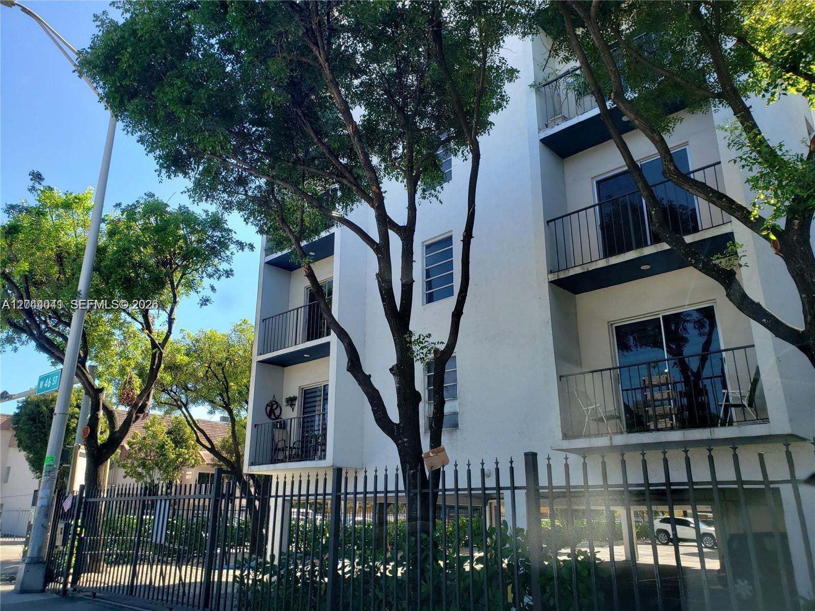 A multi-story white apartment building features balconies and is surrounded by trees and fencing — 4550 W 16th Ave # 301, Hialeah FL 33012, HIALEAH, FL