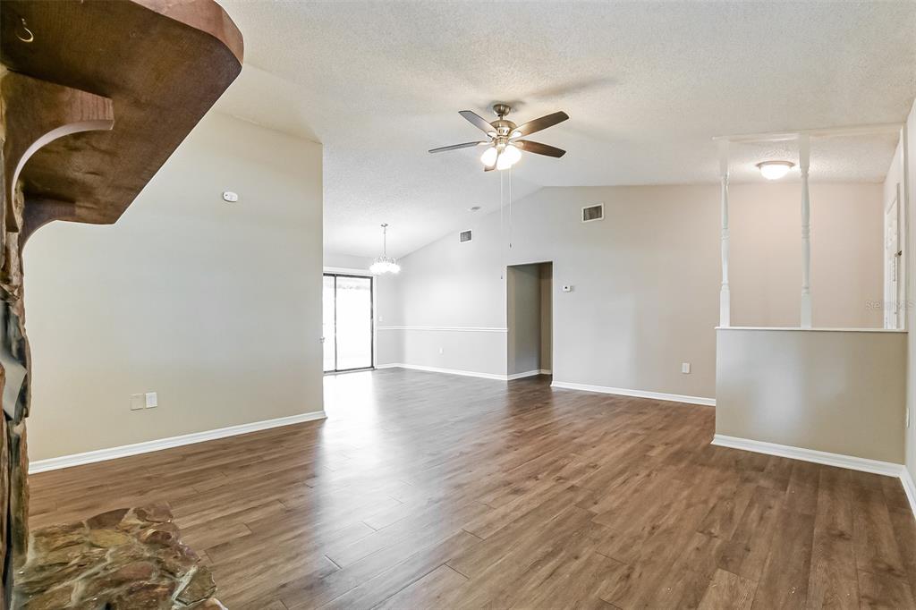 An open-concept living area features wood-look flooring, a vaulted ceiling, and a stone fireplace — 1309 COVE PLACE, TAVARES, FL