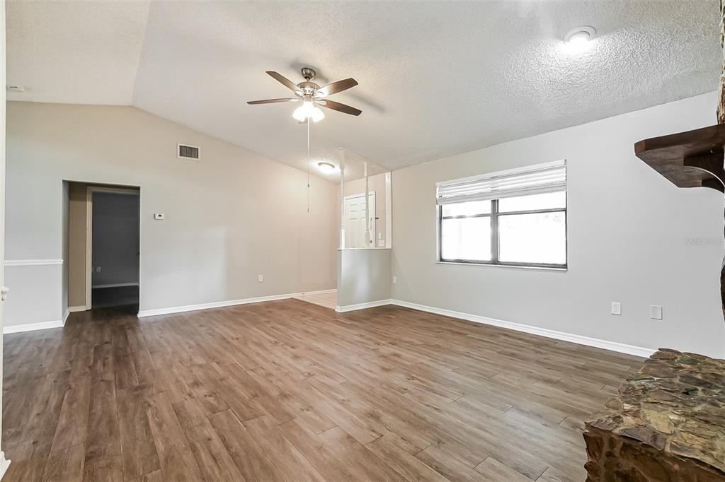 An empty living room features vaulted ceilings, wood-look flooring, and a stone fireplace hearth — 1309 COVE PLACE, TAVARES, FL