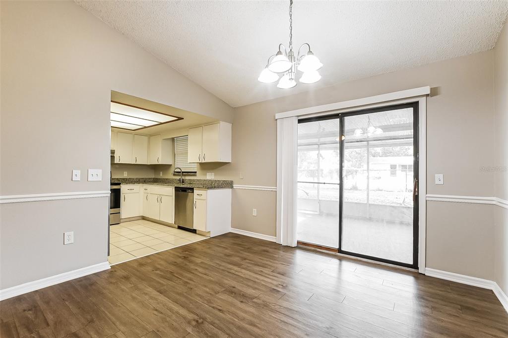 A dining area with wood-look flooring leads into a kitchen with white cabinets and appliances — 1309 COVE PLACE, TAVARES, FL