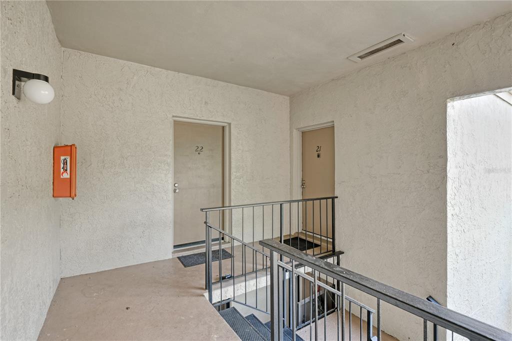 An outdoor apartment hallway features two unit doors, a metal railing, and a fire extinguisher — 3282 S SEMORAN BOULEVARD UNIT 22, ORLANDO, FL