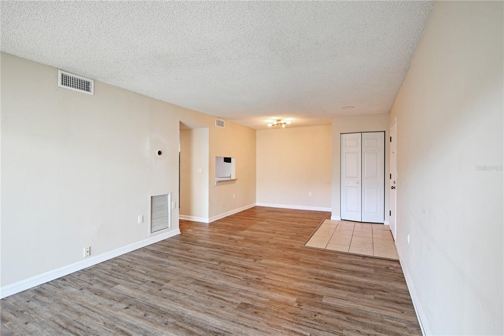 An empty living room features wood-look flooring, a tiled entryway, and a pass-through window — 3282 S SEMORAN BOULEVARD UNIT 22, ORLANDO, FL