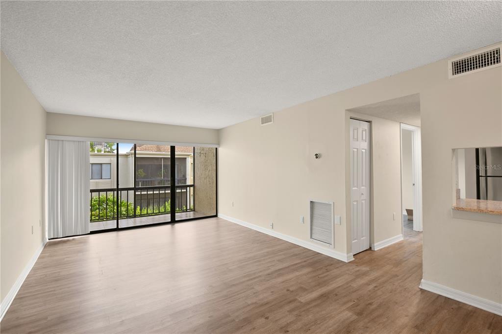 An empty living room features light wood-look flooring, beige walls, and a sliding glass balcony door — 3282 S SEMORAN BOULEVARD UNIT 22, ORLANDO, FL