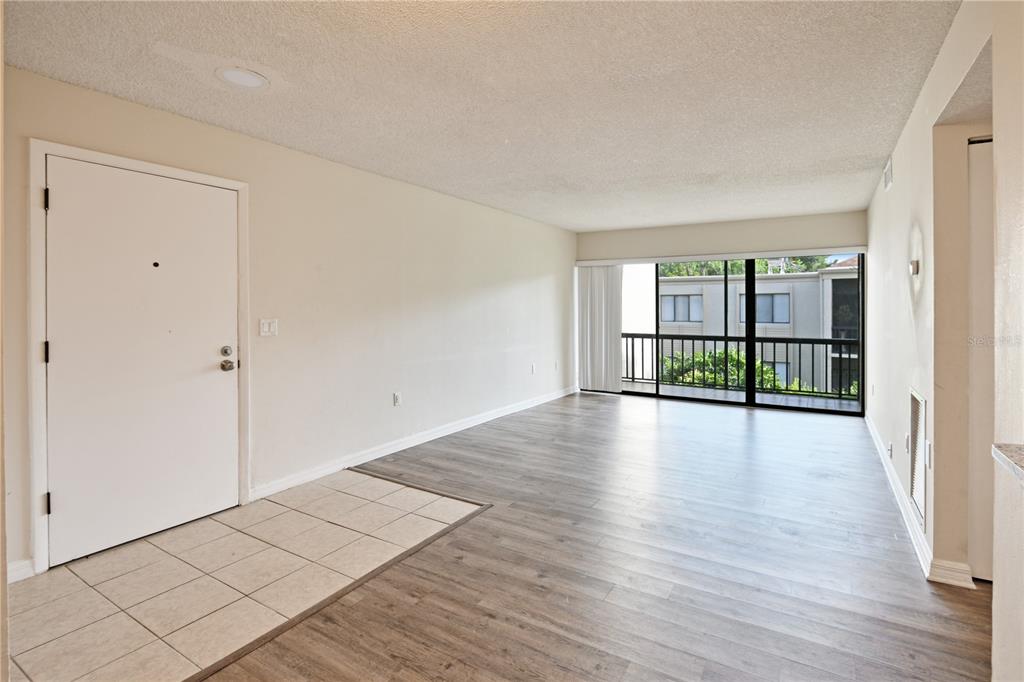 An empty living room features light-colored walls, wood-look flooring, a tiled entryway, and a balcony — 3282 S SEMORAN BOULEVARD UNIT 22, ORLANDO, FL