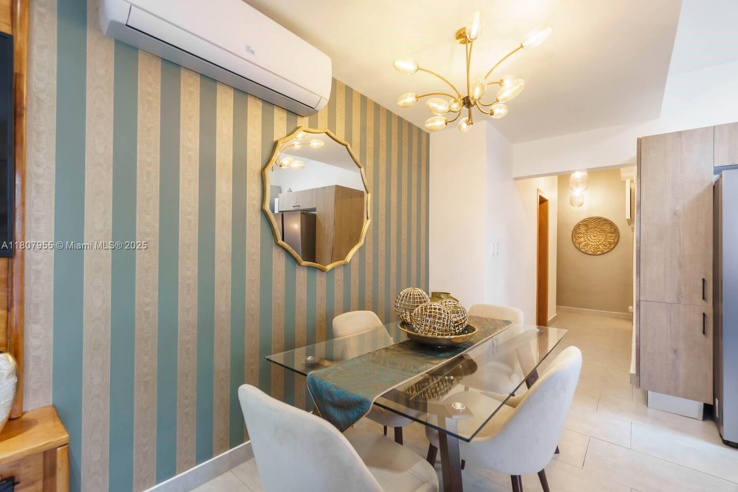 A dining room features a glass table, striped wallpaper, a gold mirror, and a chandelier — Julio Aibar #39 Suites By Refa Piantini # 401, RD, RD