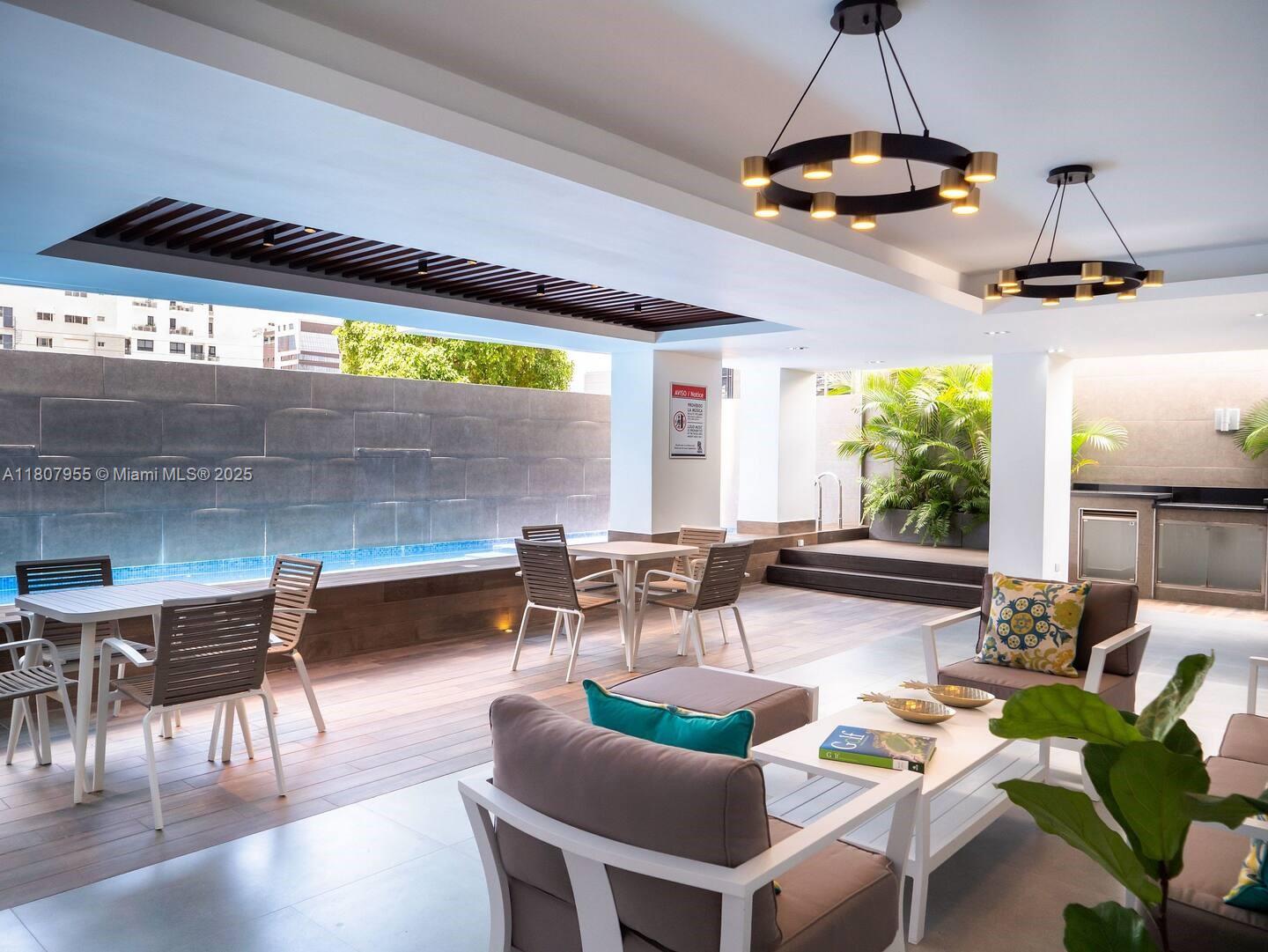 An outdoor lounge area features a swimming pool, dining tables, and modern seating under lights — Julio Aibar #39 Suites By Refa Piantini # 401, RD, RD
