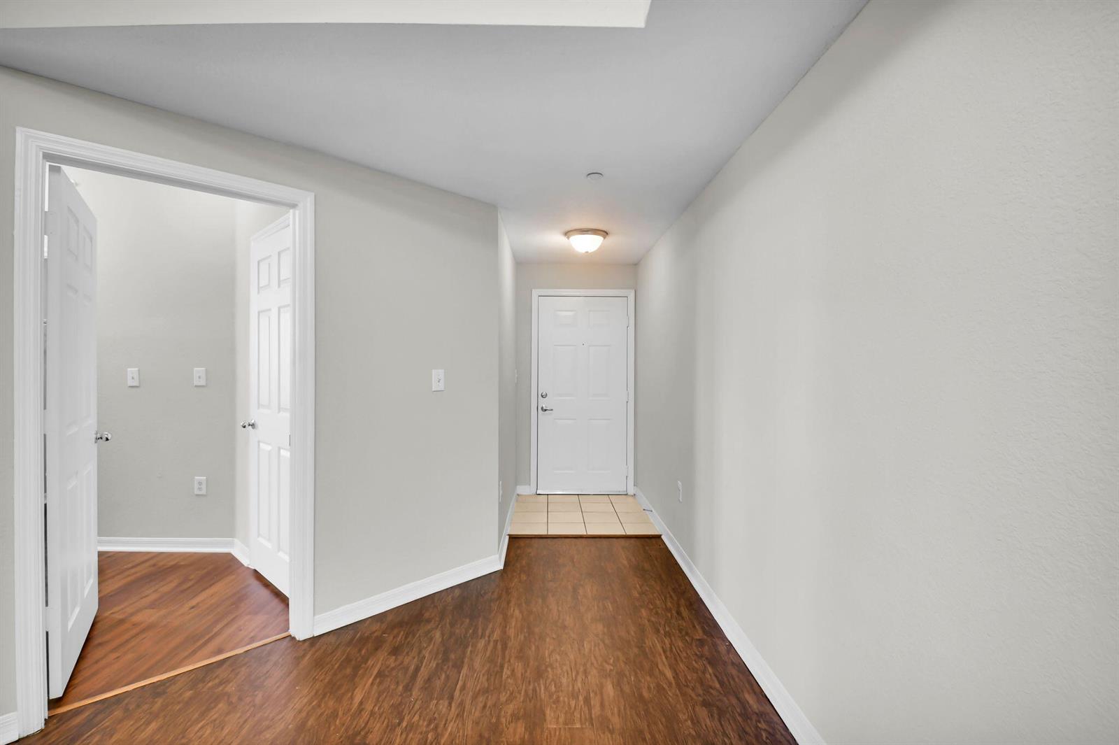 An entryway features wood-look flooring, light gray walls, and a white door with tiled flooring — 15165 Michelangelo Boulevard # 106, Delray Beach FL 33446, DELRAY BEACH, FL