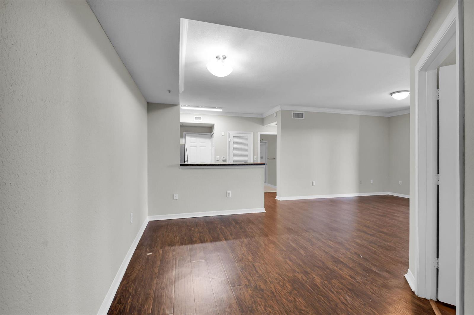 An empty living area with wood-look flooring, light gray walls, and a kitchen pass-through window — 15165 Michelangelo Boulevard # 106, Delray Beach FL 33446, DELRAY BEACH, FL