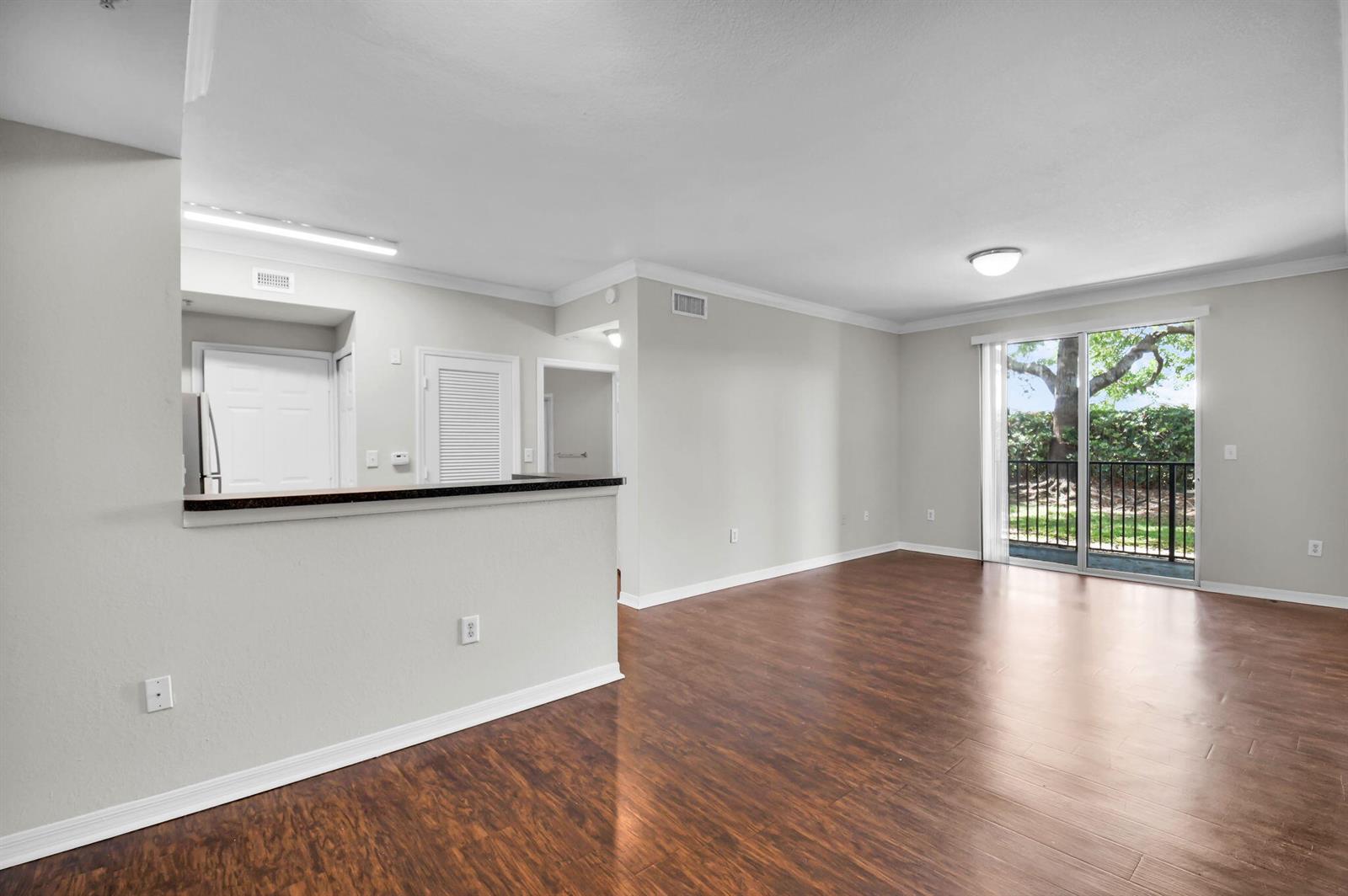An open-concept living area features wood-look flooring, a kitchen pass-through, and a sliding glass door — 15165 Michelangelo Boulevard # 106, Delray Beach FL 33446, DELRAY BEACH, FL