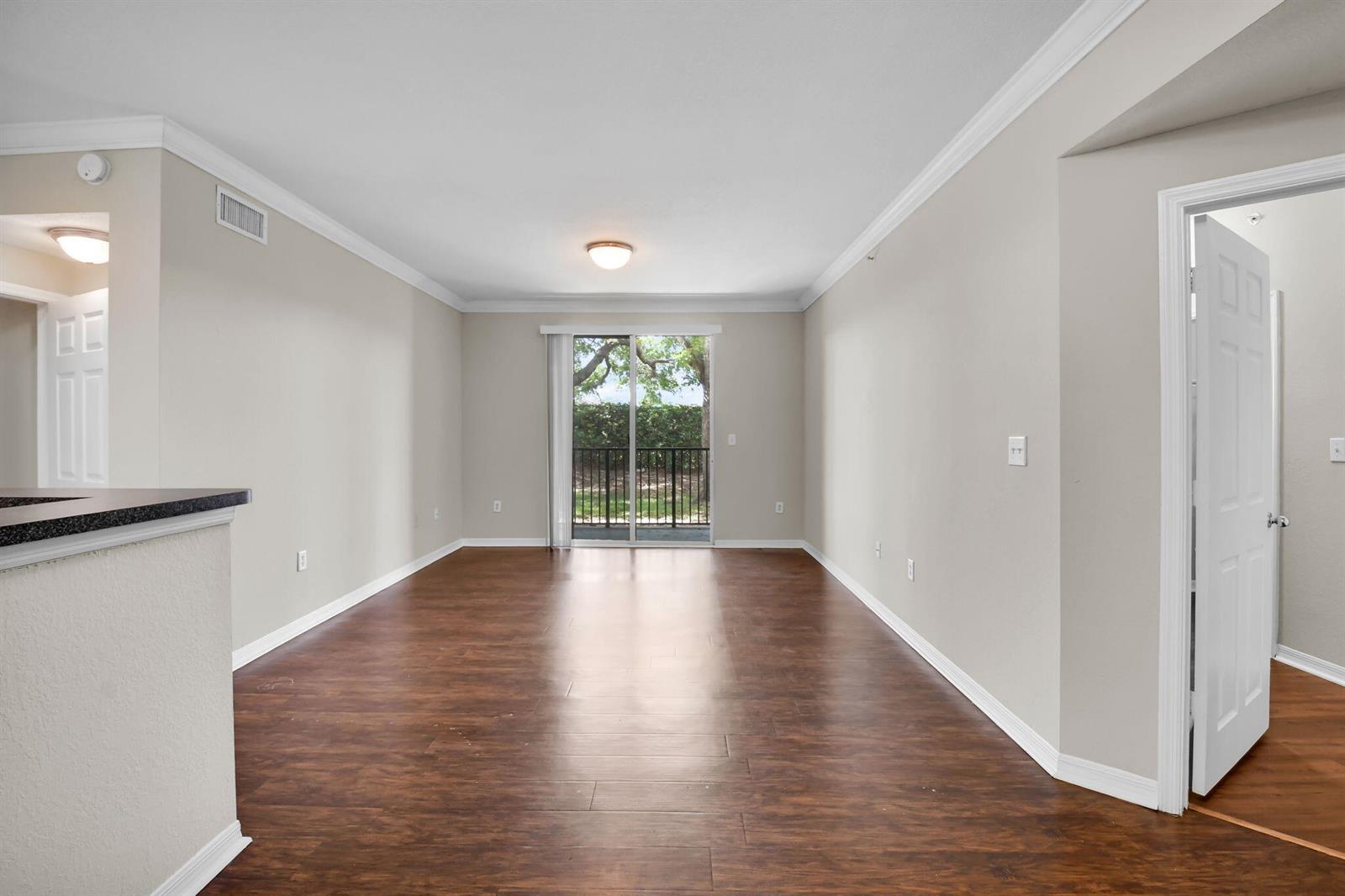 An empty living room with wood-look flooring, crown molding, and a sliding glass balcony door — 15165 Michelangelo Boulevard # 106, Delray Beach FL 33446, DELRAY BEACH, FL