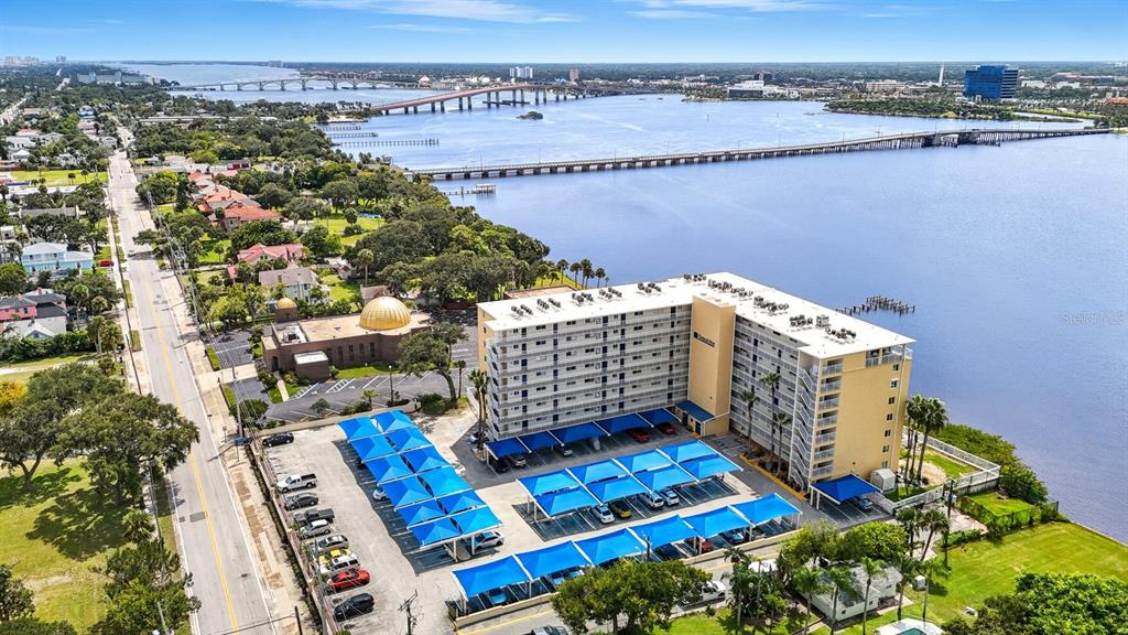 An aerial view shows a multi-story apartment building with covered parking next to a bay — 145 N HALIFAX AVENUE UNIT 405, DAYTONA BEACH, FL