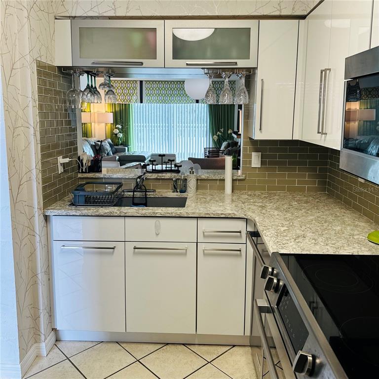 A kitchen features white cabinets, a granite countertop, a subway tile backsplash, and a pass-through window — 145 N HALIFAX AVENUE UNIT 405, DAYTONA BEACH, FL