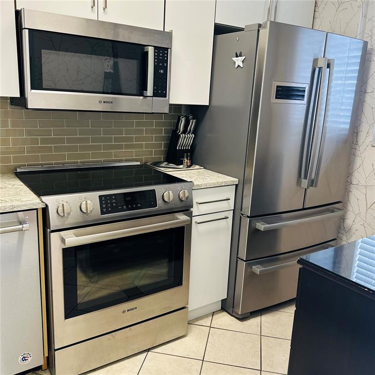 A kitchen features stainless steel appliances, white cabinets, and a light-colored tiled backsplash — 145 N HALIFAX AVENUE UNIT 405, DAYTONA BEACH, FL