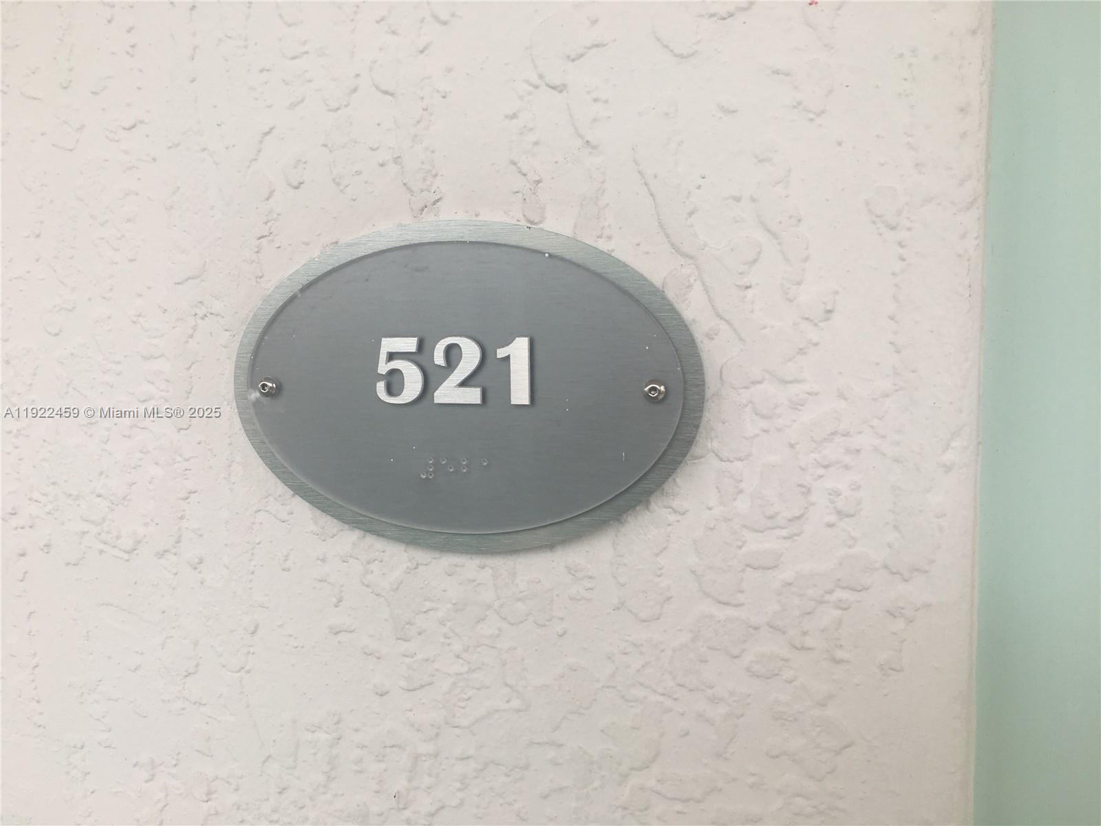 An oval sign with the number 521 and braille is mounted on a textured wall — 6000 Collins Ave # 521, Miami Beach FL 33140, MIAMI BEACH, FL
