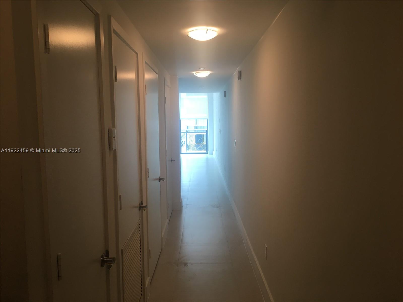 A narrow hallway with white walls, tile flooring, and several closed doors leads toward a balcony — 6000 Collins Ave # 521, Miami Beach FL 33140, MIAMI BEACH, FL