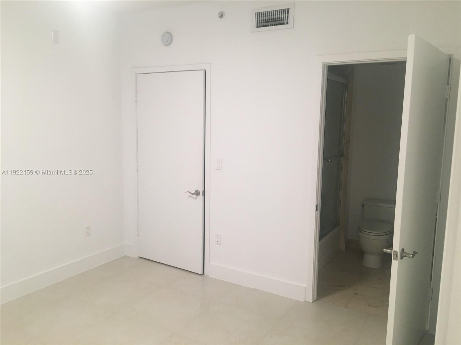 A room with white walls, tile flooring, a closed door, and an open bathroom door — 6000 Collins Ave # 521, Miami Beach FL 33140, MIAMI BEACH, FL