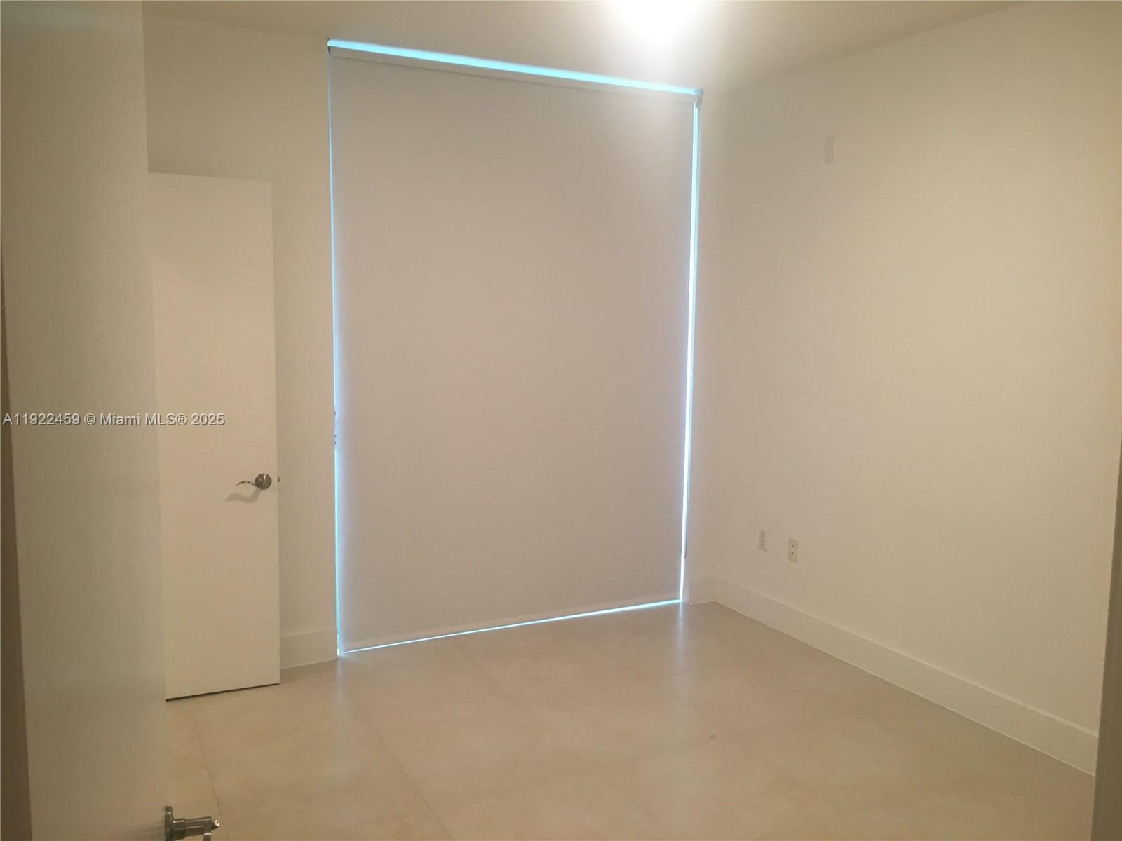 An empty room features white walls, light-colored tile flooring, and a large window with shades — 6000 Collins Ave # 521, Miami Beach FL 33140, MIAMI BEACH, FL
