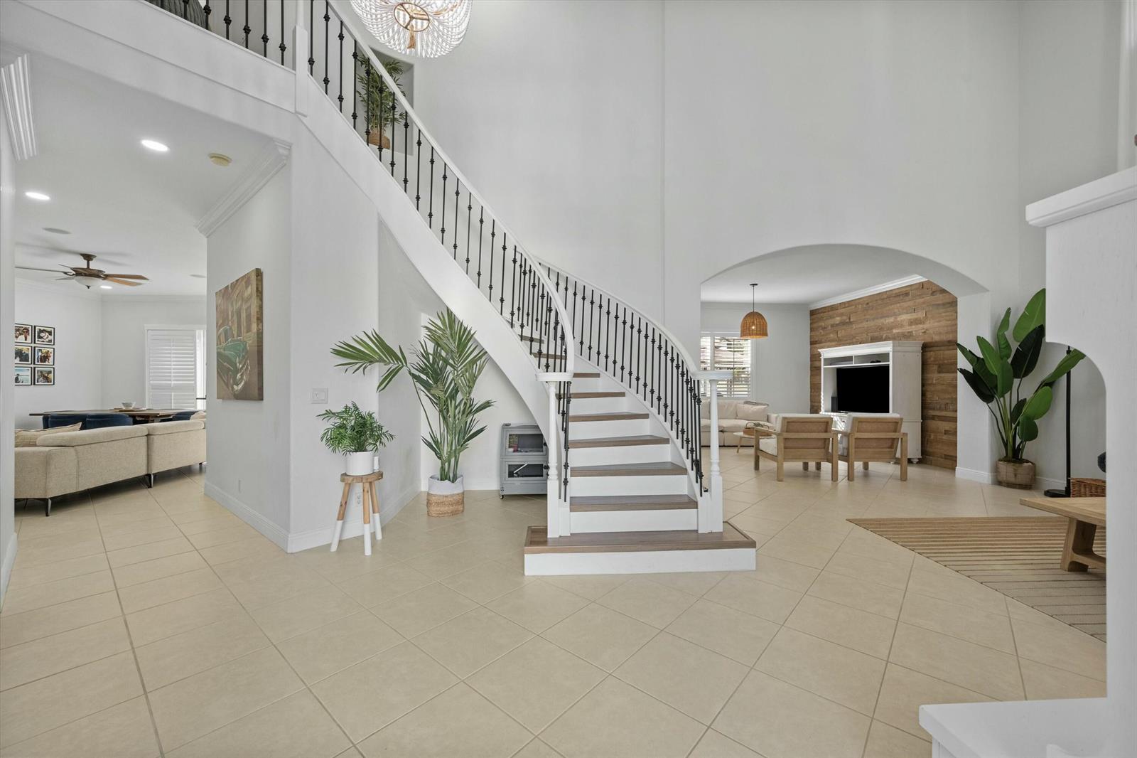 A bright, open-concept foyer features a curved staircase, tile flooring, and a view into living areas — 1386 Beacon Circle, Wellington FL 33414, WELLINGTON, FL