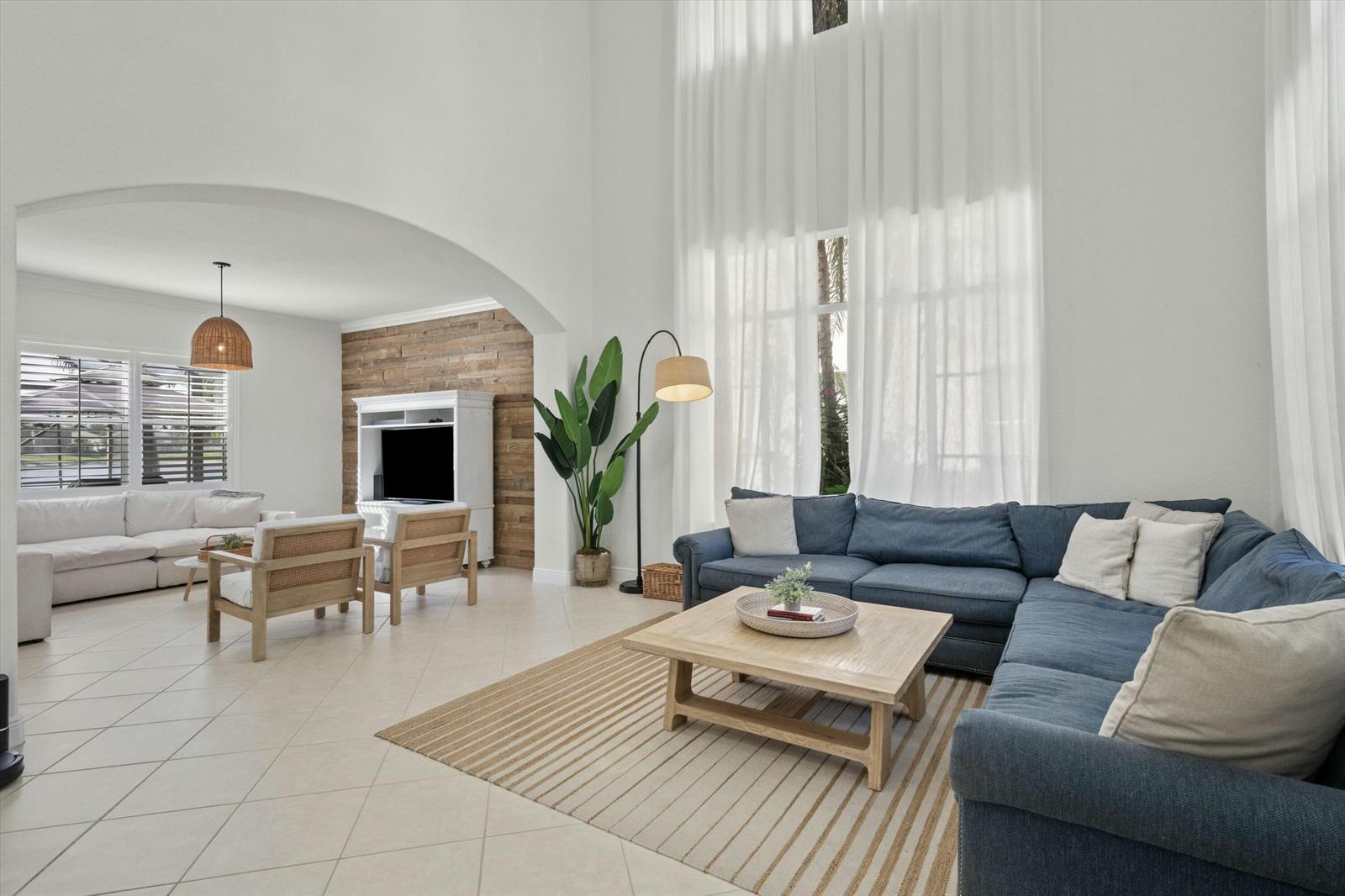 A spacious living room features a blue sectional sofa, wood coffee table, and high ceilings — 1386 Beacon Circle, Wellington FL 33414, WELLINGTON, FL