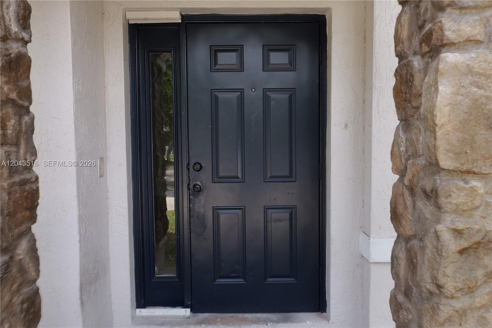 A dark-colored front door with a side light window is framed by stone pillars — 8220 SW 25th Ct, Miramar FL 33025, MIRAMAR, FL