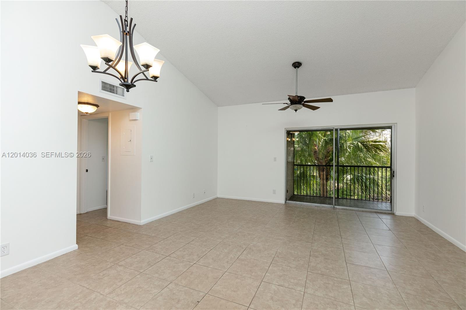 An empty living room features tile flooring, a vaulted ceiling, a chandelier, and a balcony — 717 Gardens Dr # 201, Pompano Beach FL 33069, POMPANO BEACH, FL