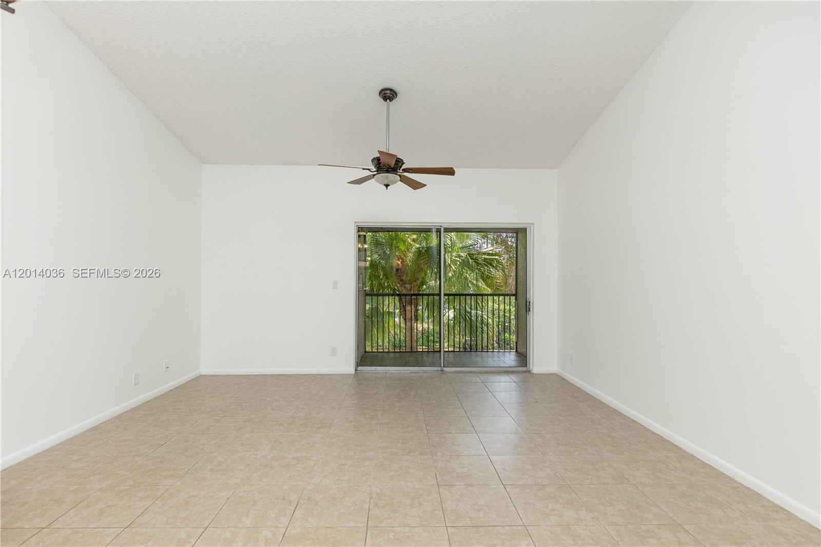 An empty room features beige tile flooring, white walls, a ceiling fan, and a sliding glass door — 717 Gardens Dr # 201, Pompano Beach FL 33069, POMPANO BEACH, FL