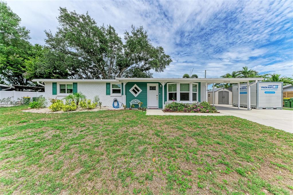 A single-story white brick house with teal trim and a carport under a blue sky — 2317 S TUTTLE AVENUE, SARASOTA, FL