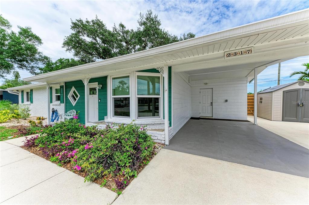 A white house with green accents features a front carport, a walkway, and landscaping — 2317 S TUTTLE AVENUE, SARASOTA, FL