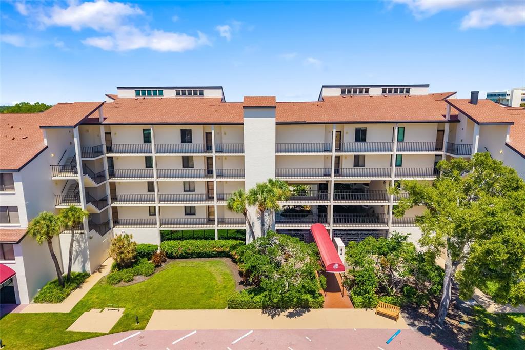 An aerial view shows the exterior of a multi-story apartment building with a red awning — 6263 MIDNIGHT PASS ROAD UNIT 403, SARASOTA, FL