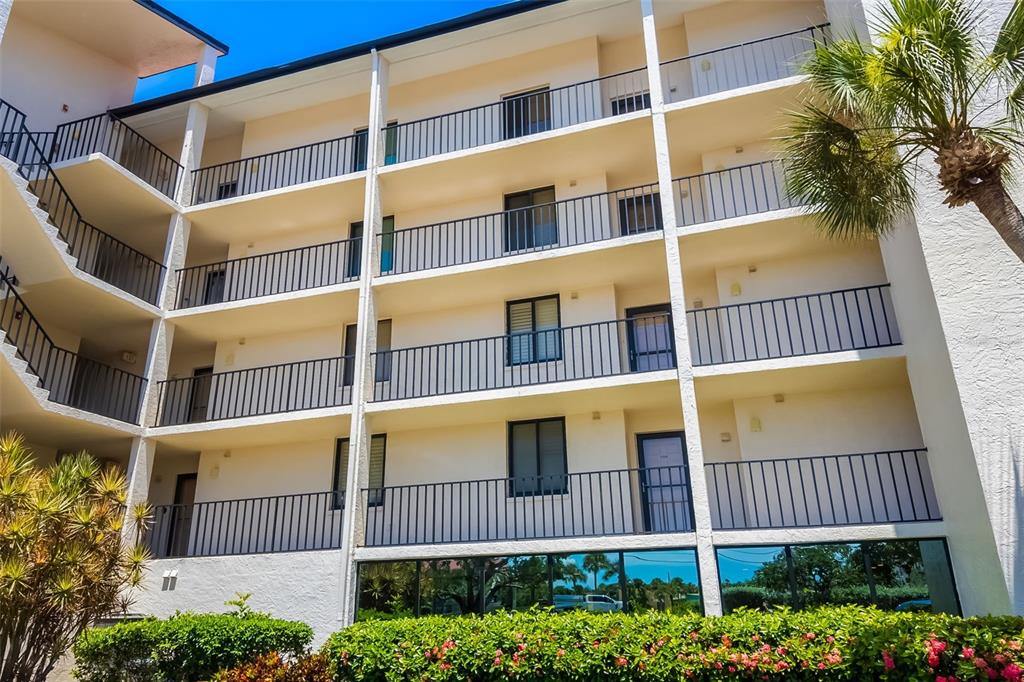 A multi-story apartment building exterior features balconies with black railings and a ground-level glass facade — 6263 MIDNIGHT PASS ROAD UNIT 403, SARASOTA, FL