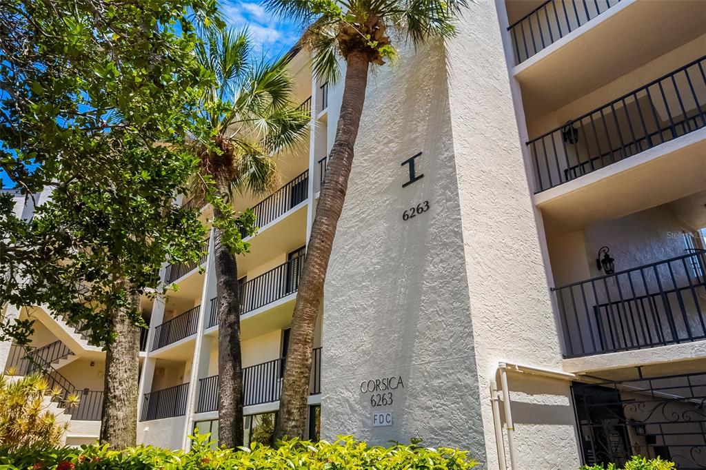 A multi-story apartment building exterior features a white stucco facade, palm trees, and balcony railings — 6263 MIDNIGHT PASS ROAD UNIT 403, SARASOTA, FL