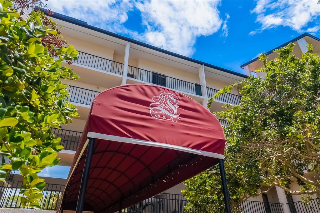A red fabric awning with a white logo stands before a multi-story apartment building — 6263 MIDNIGHT PASS ROAD UNIT 403, SARASOTA, FL