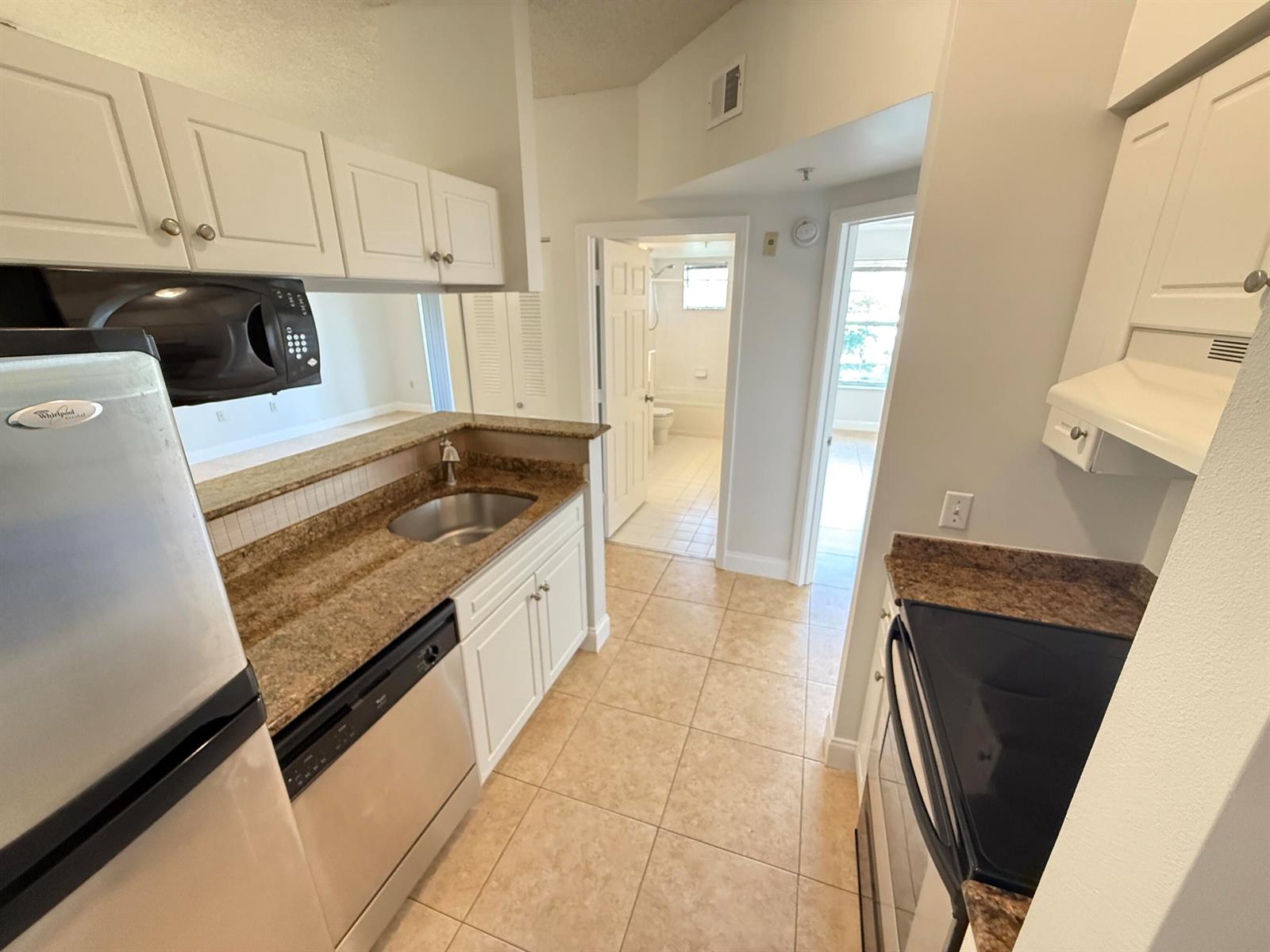 A galley kitchen features white cabinets, granite countertops, stainless steel appliances, and tile flooring — 1407 Tuscany Way # 1407, Boynton Beach FL 33435, BOYNTON BEACH, FL