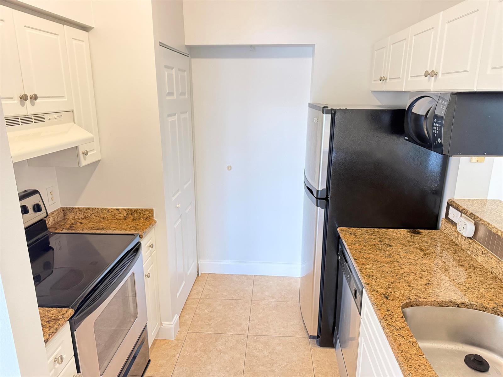 A kitchen features white cabinets, granite countertops, stainless steel appliances, and beige tile flooring — 1407 Tuscany Way # 1407, Boynton Beach FL 33435, BOYNTON BEACH, FL