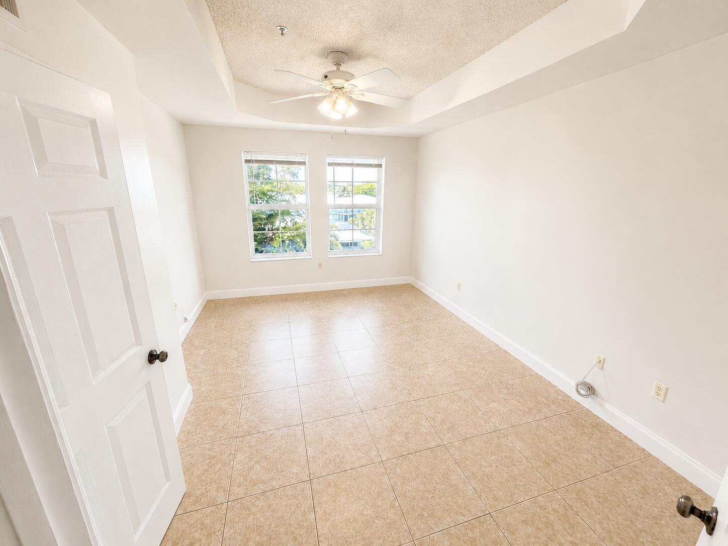 An empty bedroom features beige tile flooring, a tray ceiling with a fan, and two windows — 1407 Tuscany Way # 1407, Boynton Beach FL 33435, BOYNTON BEACH, FL