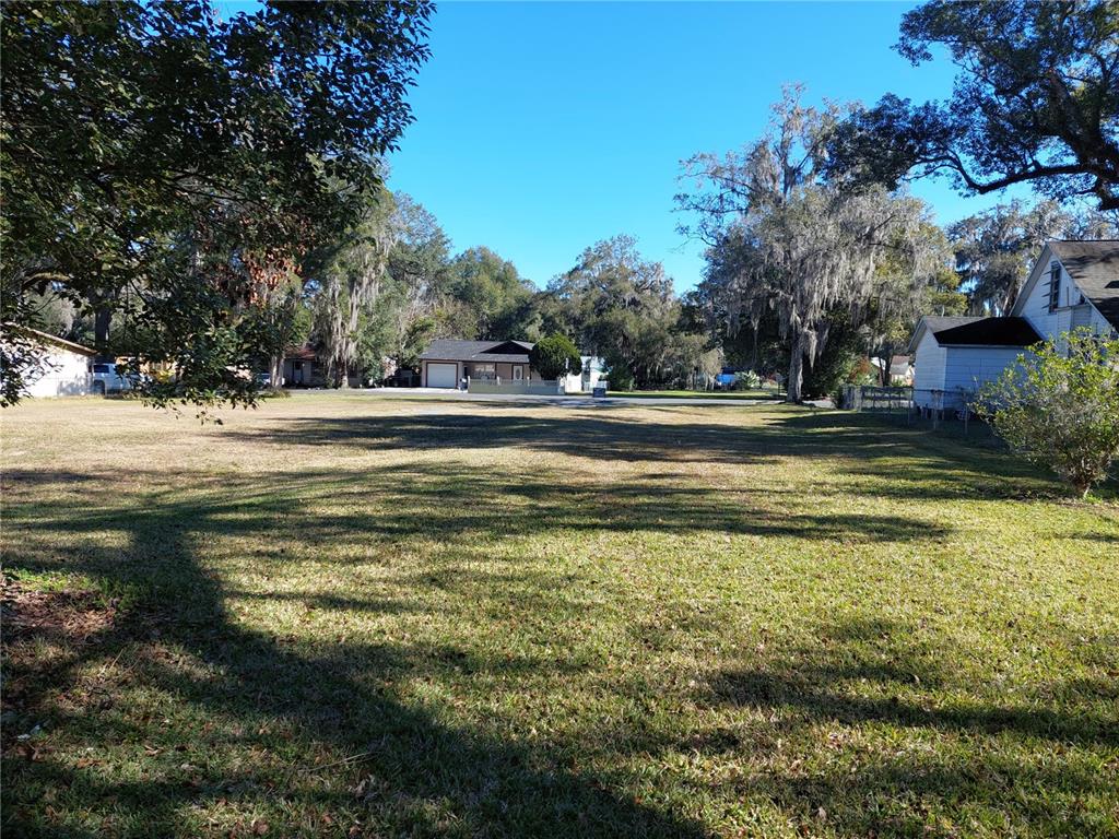 A large, grassy vacant lot is surrounded by mature trees and neighboring residential houses — 5449 12TH STREET, ZEPHYRHILLS, FL